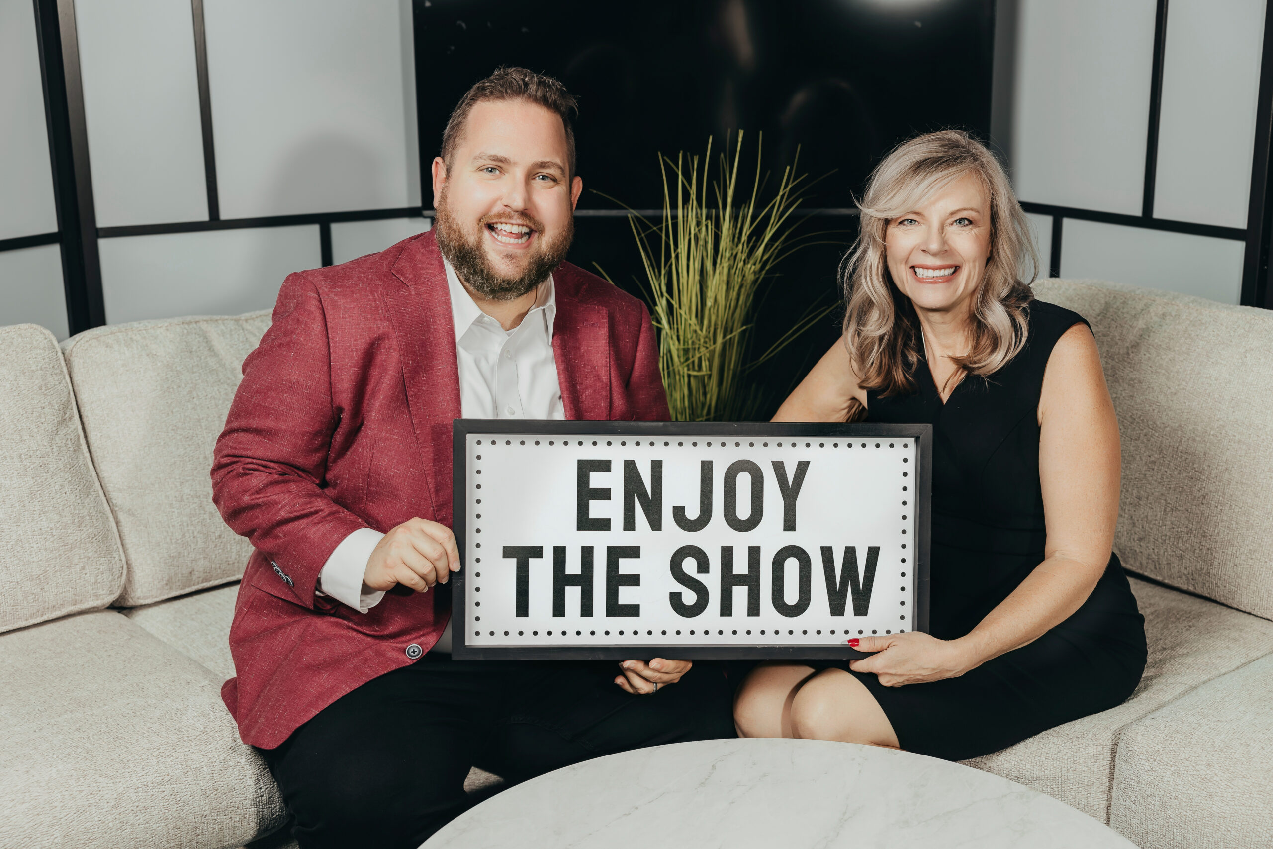 Tommy Whitehead and Shirley Jump on the Building Success Productions studio set holding an Enjoy the Show sign
